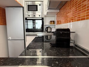 Een keuken met een koelkast, magnetron, oven en koffieapparaat.
