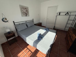 Ein Schlafzimmer mit Bett, Nachttisch, Lampe, Wanddekoration, Kleiderschrank und einer Tür.