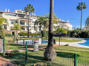 Ein Resort mit Swimmingpool, Palmen und einem umzäunten Bereich mit Rettungsschwimmerstuhl.