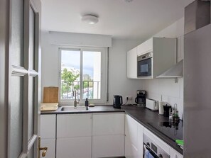 Eine moderne Küche mit weißen Schränken, einer schwarzen Arbeitsplatte, einem Fenster mit Blick und einer eingebauten Mikrowelle.