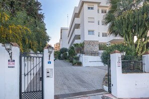 A gated entrance to a residential building with a paved driveway, a stone wall, and a blue sign indicating the entrance. - Calm and bright 1bedroom with Terrace & pool views (Mijas)