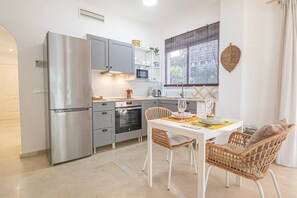 Een moderne keuken met roestvrijstalen apparatuur, een eethoek met rieten stoelen en een raam met uitzicht.