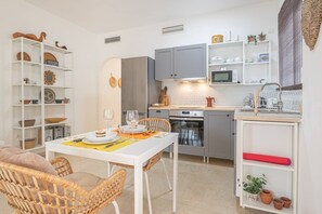 Een kleine keuken met een eethoek, witte kasten, een magnetron en een kleine eettafel gedekt met borden en glazen.