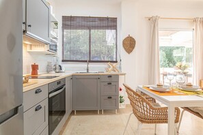 A compact kitchen with a dining area, a window with a view, and a decorative leaf on the wall. - Calm and bright 1bedroom with Terrace & pool views (Mijas)