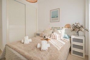 A bedroom with a large bed, a nightstand, a bedside table, a wall-mounted shelf, and a framed picture. - Calm and bright 1bedroom with Terrace & pool views (Mijas)