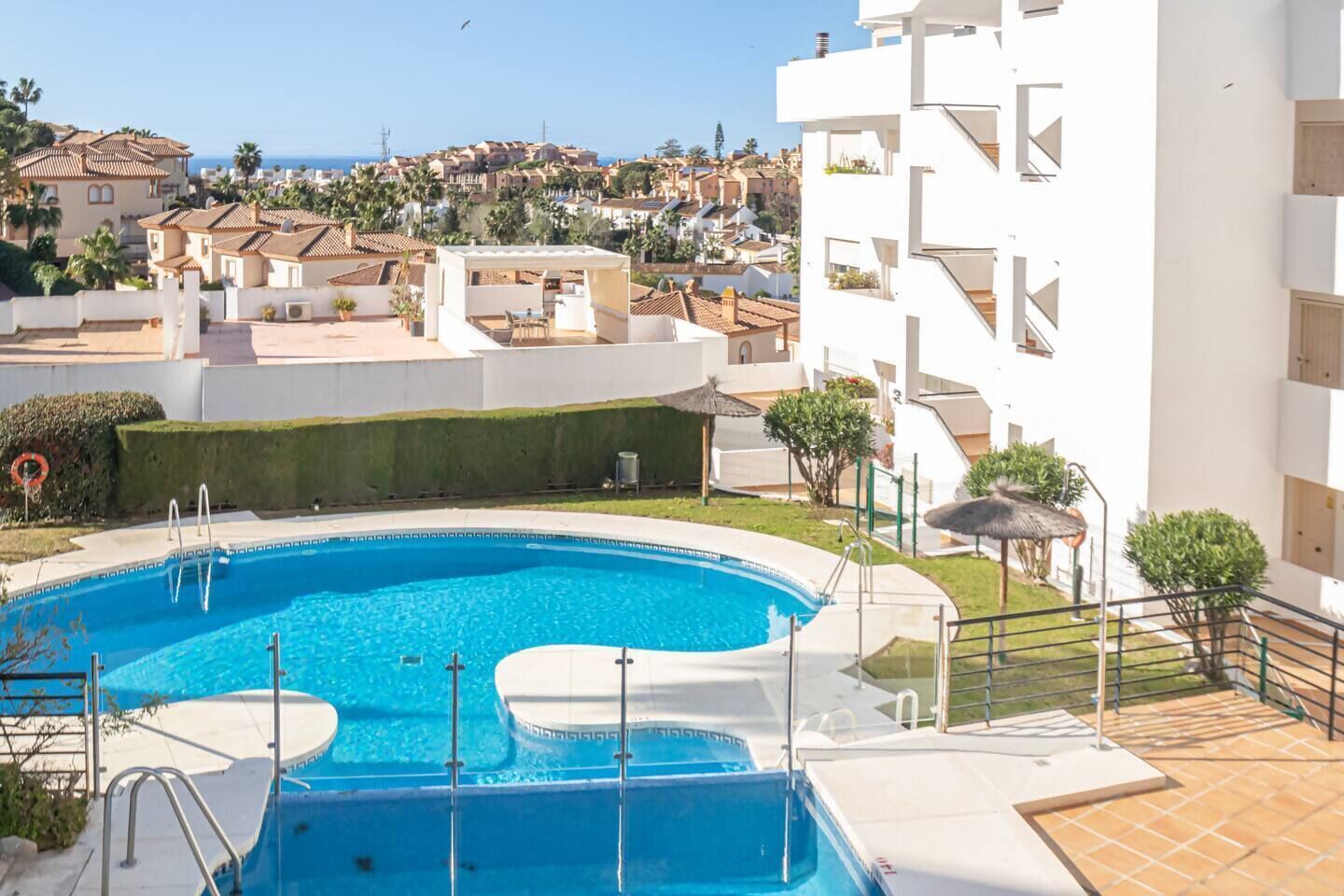 Una piscina con vistas a un pueblo costero, rodeada de edificios blancos y un cielo despejado.