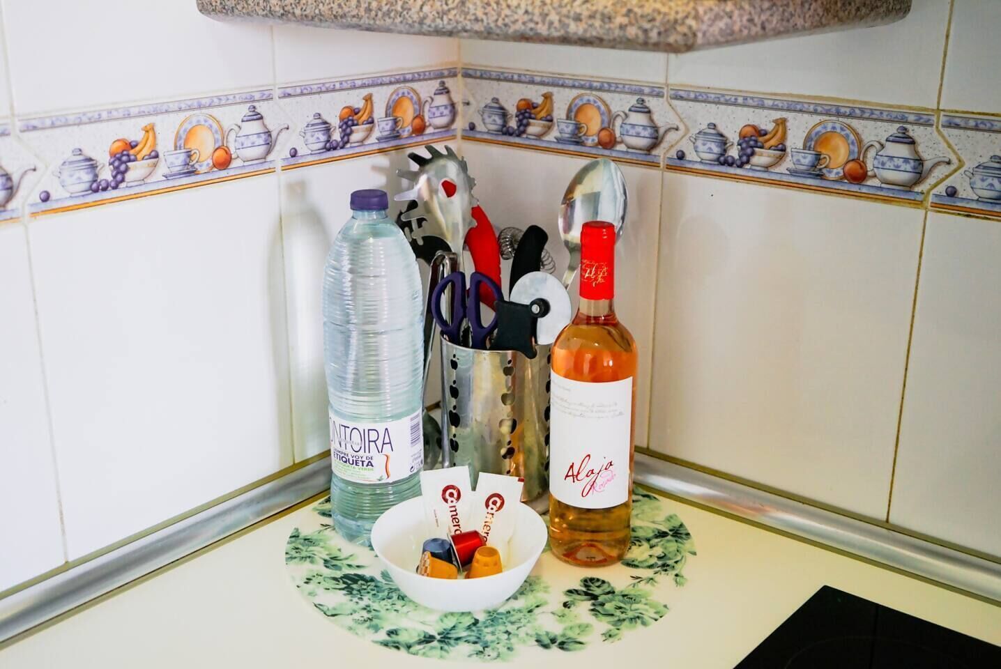 Een aanrecht met een waterfles, een fles wijn, een schaal met snacks en keukengerei.
