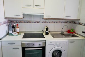 A compact kitchen with a dishwasher, washing machine, sink, and a small countertop with a water dispenser and a bottle. - Bright & quiet 2 bedroom with large terrace & pool (Mijas)