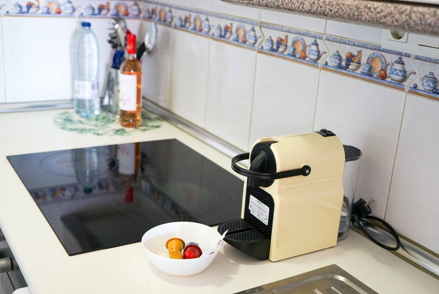 A kitchen with a stove, a coffee maker, and a bowl with fruits.