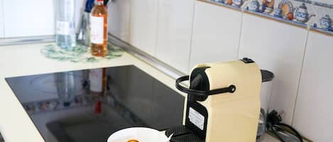 A kitchen with a stove, a coffee maker, and a bowl with fruits.