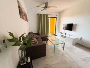 A modern living room with a sofa, a glass coffee table, a TV, and a ceiling fan. - Bright & quiet 2 bedroom with large terrace & pool (Mijas)