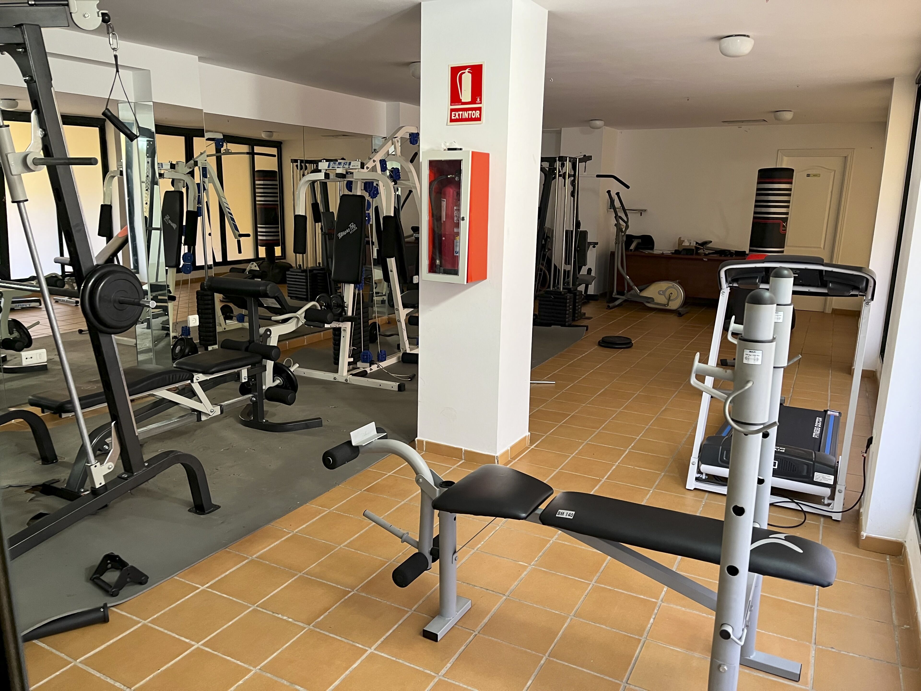 A gym with various exercise equipment, including a bench press, dumbbells, and weight machines.