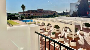 Terraço no telhado com colunas brancas, piscina e vista de edifícios ao fundo.