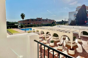 Eine Dachterrasse mit weißen Säulen, einem Schwimmbecken und Blick auf Gebäude im Hintergrund.
