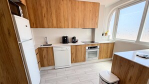 Uma cozinha moderna com armários de madeira, lava-louças, forno e janela que traz luz natural.