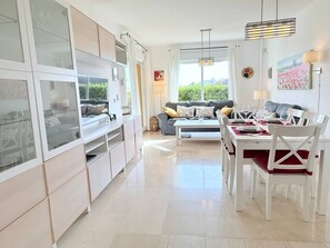 A modern kitchen with white cabinetry, a dining area with a white table and chairs, and a sofa in the background. - Two bedroom Garden Apt with Sea Views & Pool (Mijas)