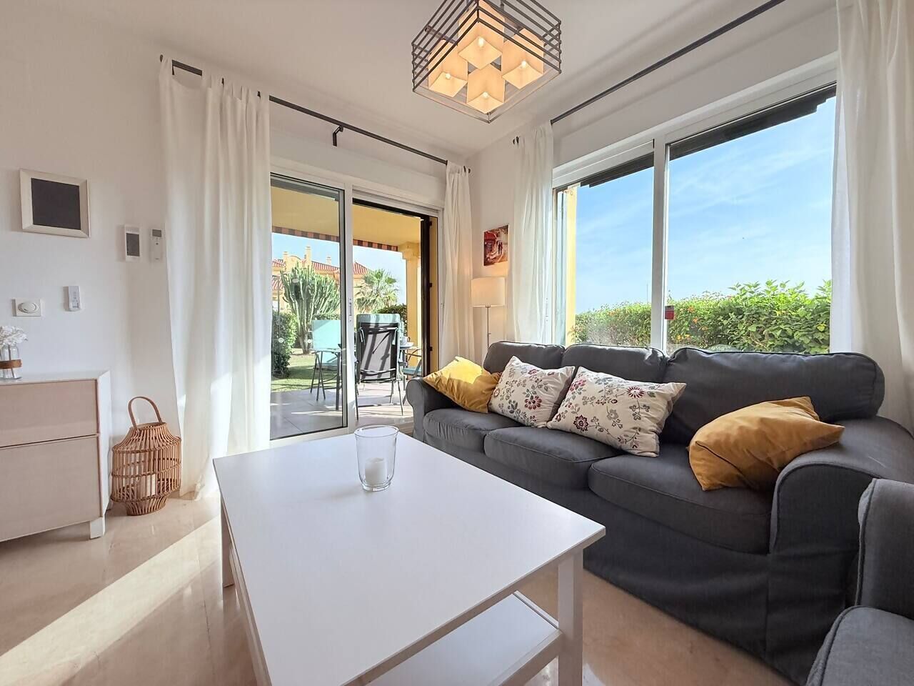 A modern living room with a sofa, a coffee table, and a view through large windows.