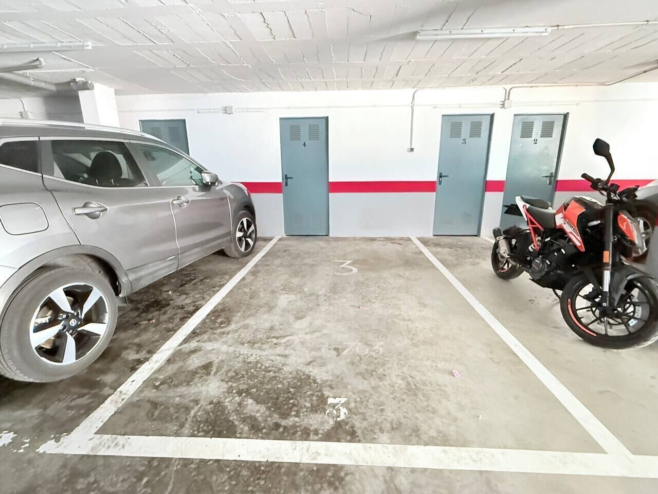 A parking garage with a car and a motorcycle, concrete floor, and doors numbered 1 to 5.