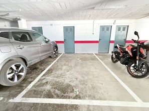 Eine Parkgarage mit einem Auto und einem Motorrad, einem Betonboden und Türen mit der Nummer 1 bis 5.