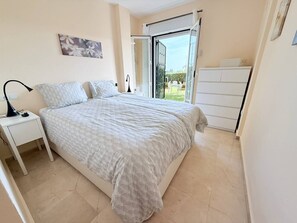 A bedroom with a bed, a nightstand, a dresser, and a sliding glass door leading to a balcony. - Two bedroom Garden Apt with Sea Views & Pool (Mijas)