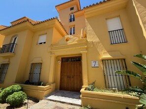 A yellow building with a wooden door, numbered 7, and a balcony with black railings. - Two bedroom Garden Apt with Sea Views & Pool (Mijas)