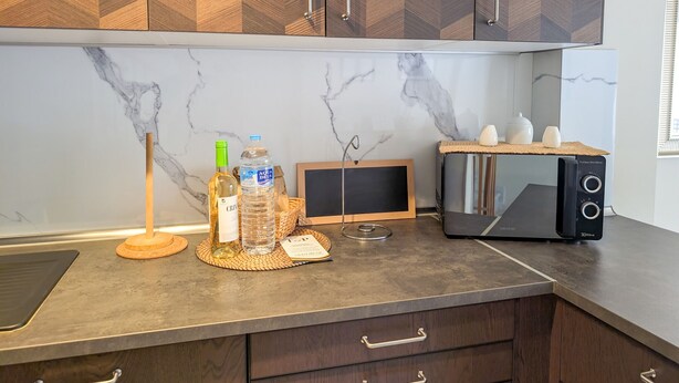 A kitchen with a marble backsplash, wooden cabinets, a toaster, a water dispenser, and a small chalkboard.