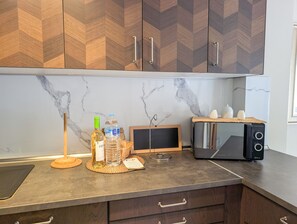 Une cuisine avec un pare-feu en marbre, des armoires en bois, un grille-pain, un distributeur d’eau et un petit tableau noir.