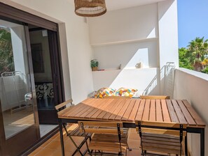 Un balcon avec une table et des chaises en bois, un luminaire suspendu en osier et une vue sur des palmiers.