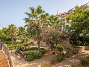 A courtyard with palm trees, a pink flowering bush, and a stone wall. - Casa Sur: Spacious & stylish 4BR by the sea (Mijas)