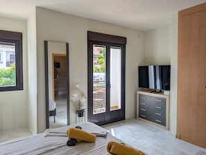 Ein Schlafzimmer mit einem Bett, einem Fernseher auf einer Holzkommode, einem Spiegel und einer Tür, die auf einen Balkon führt.