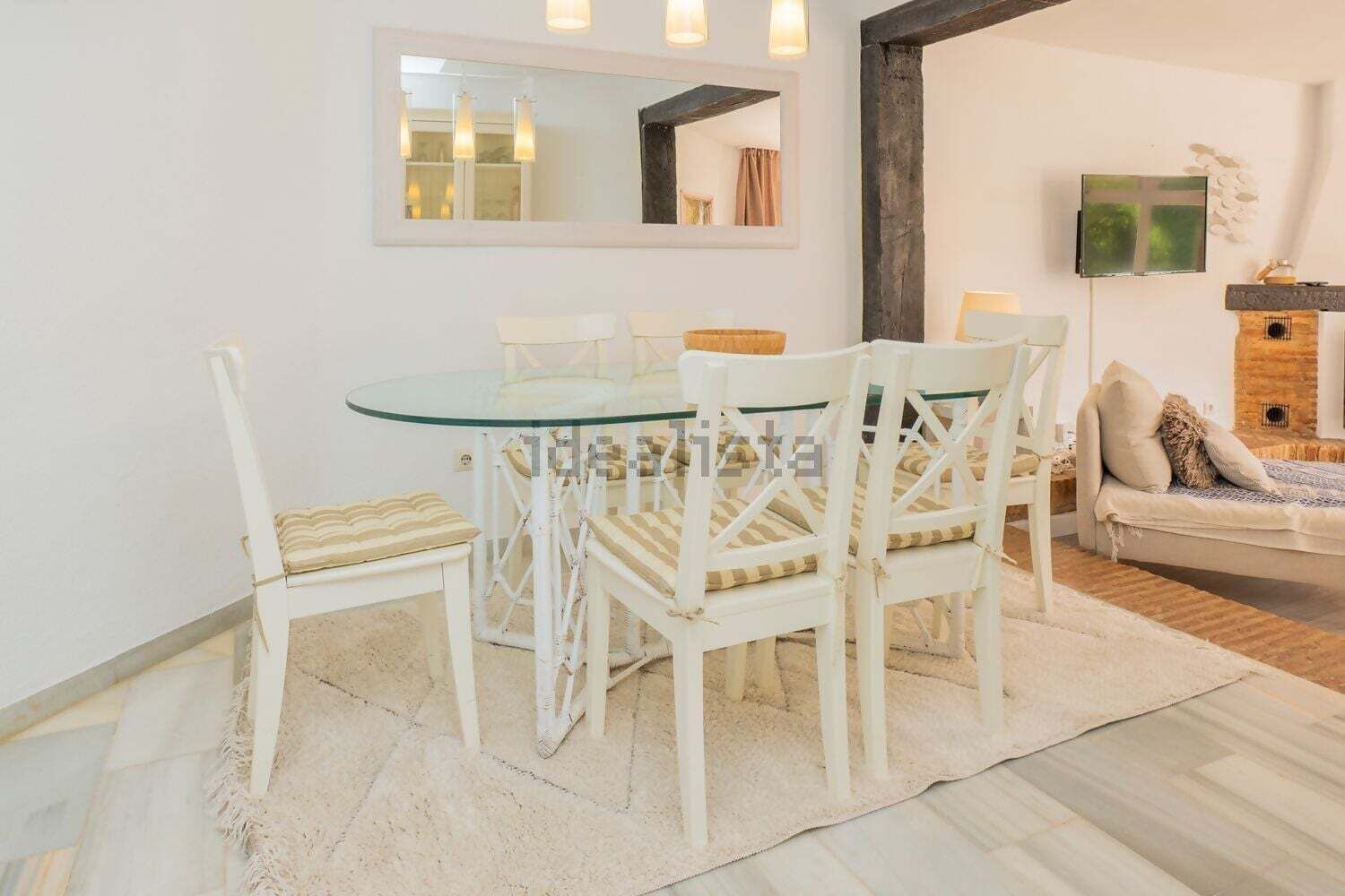 Un coin repas avec une table en verre et des chaises blanches, un canapé, une cheminée et un téléviseur fixé au mur.
