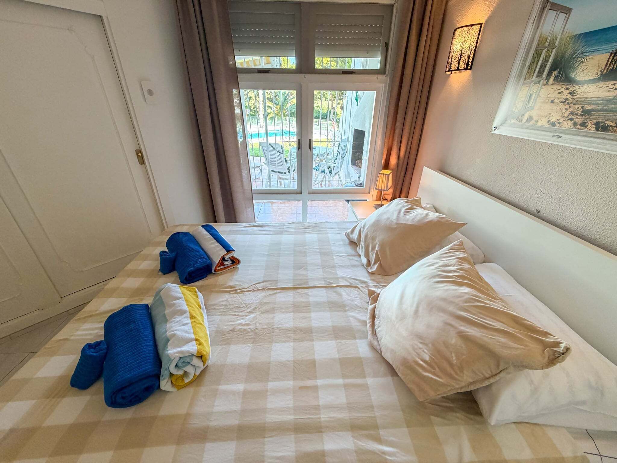 Habitación de hotel con una colcha a cuadros, dos almohadas, una toalla azul enrollada y una toalla amarilla en el suelo.