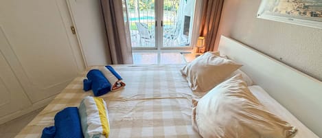 Une chambre d’hôtel avec une couvre-lit à carreaux, deux oreillers, une serviette bleue roulée et une serviette jaune sur le sol.