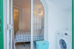 A compact room with a bed, a washing machine, and a laundry basket. - Calahonda 2BR Garden Apt · Pool · Beach Walk (Mijas)
