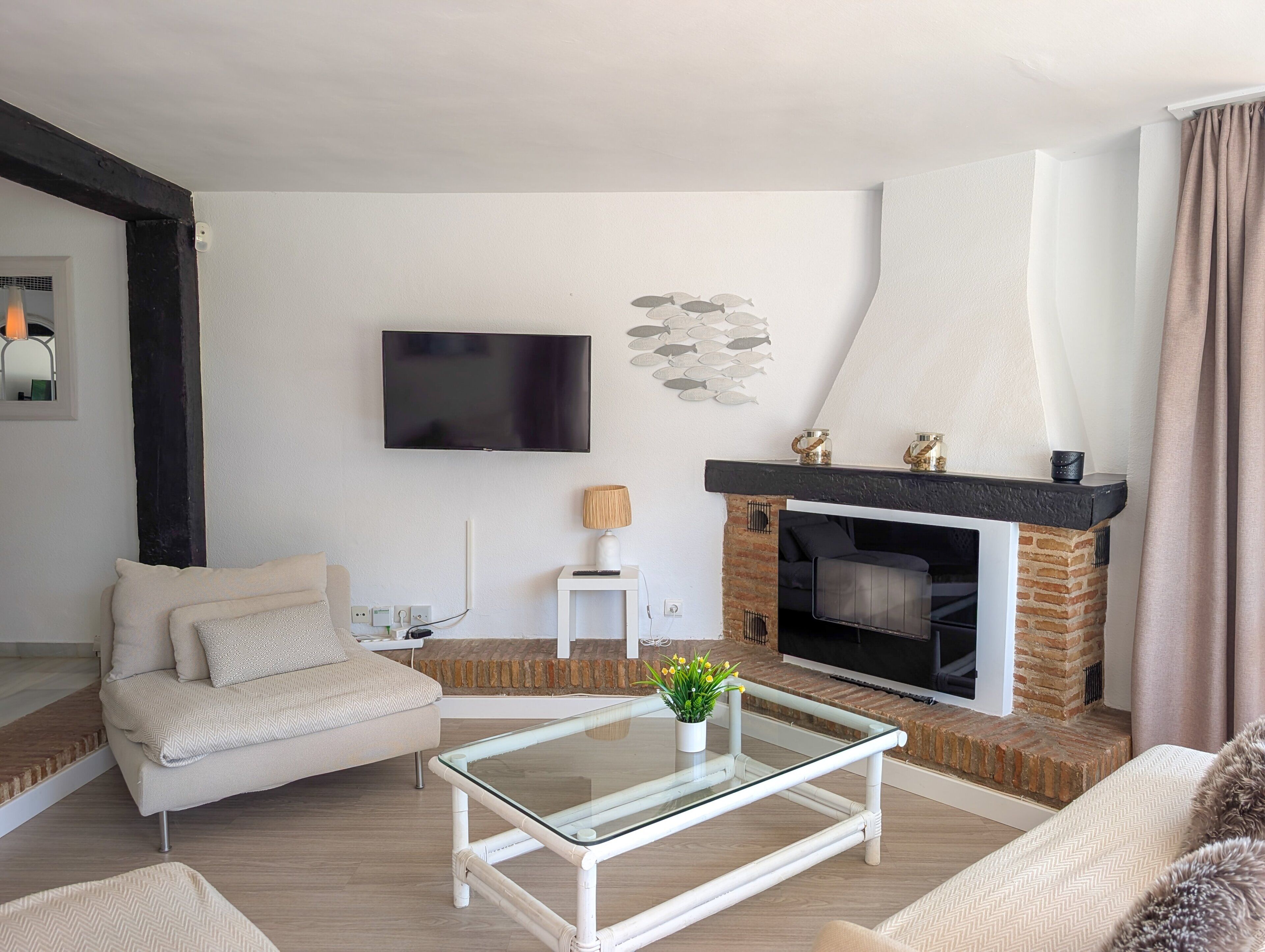A living room with a sofa, a glass coffee table, a fireplace, and a TV mounted on the wall.