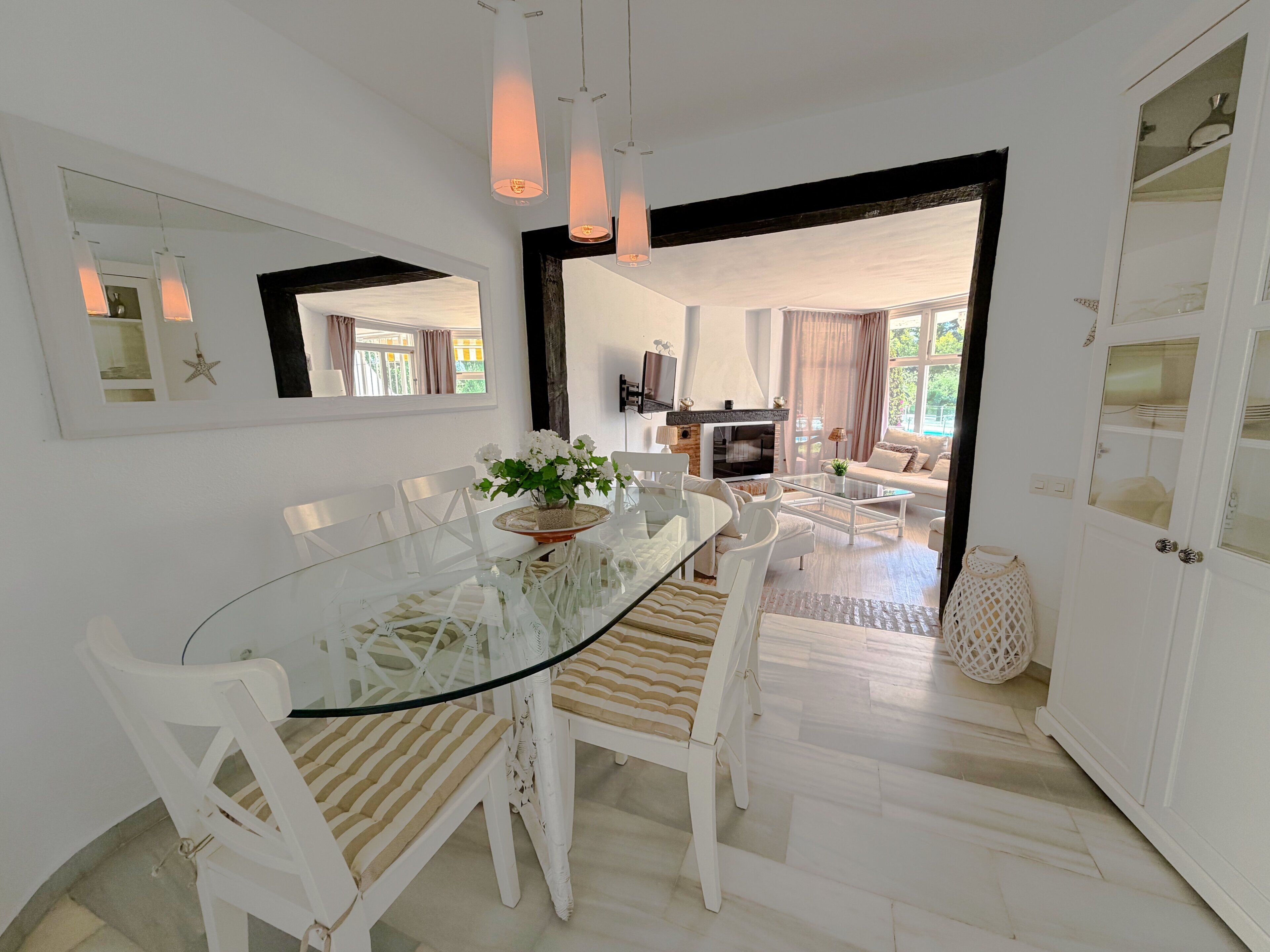Un espace repas moderne avec une table en verre, des chaises blanches et un arrangement floral central.
