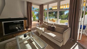Ein Wohnzimmer mit Kamin, einer Couch und großen Fenstern mit Blick auf Pool und Garten.