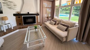 Ein Wohnzimmer mit Kamin, Sofa, Couchtisch und großen Fenstern.