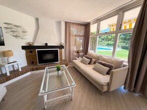 Ein Wohnzimmer mit Kamin, Sofa, Couchtisch und großen Fenstern.