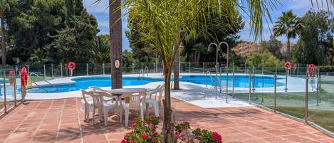 Una piscina con borde de baldosas, rodeada de palmeras y un jardín de flores.
