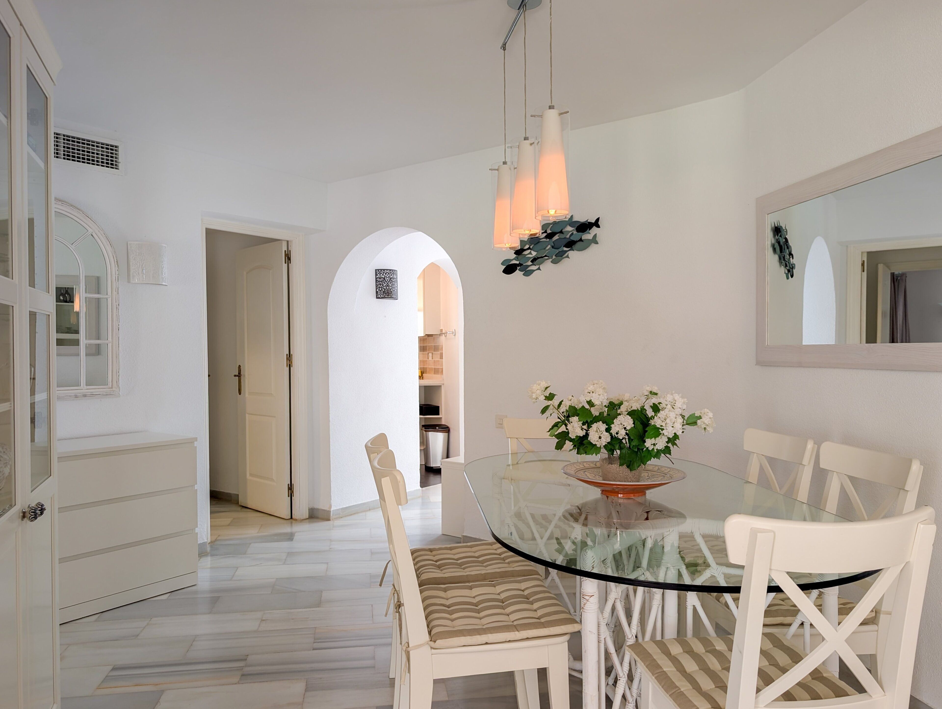 A dining area with a glass table, white chairs, and a vase of flowers.