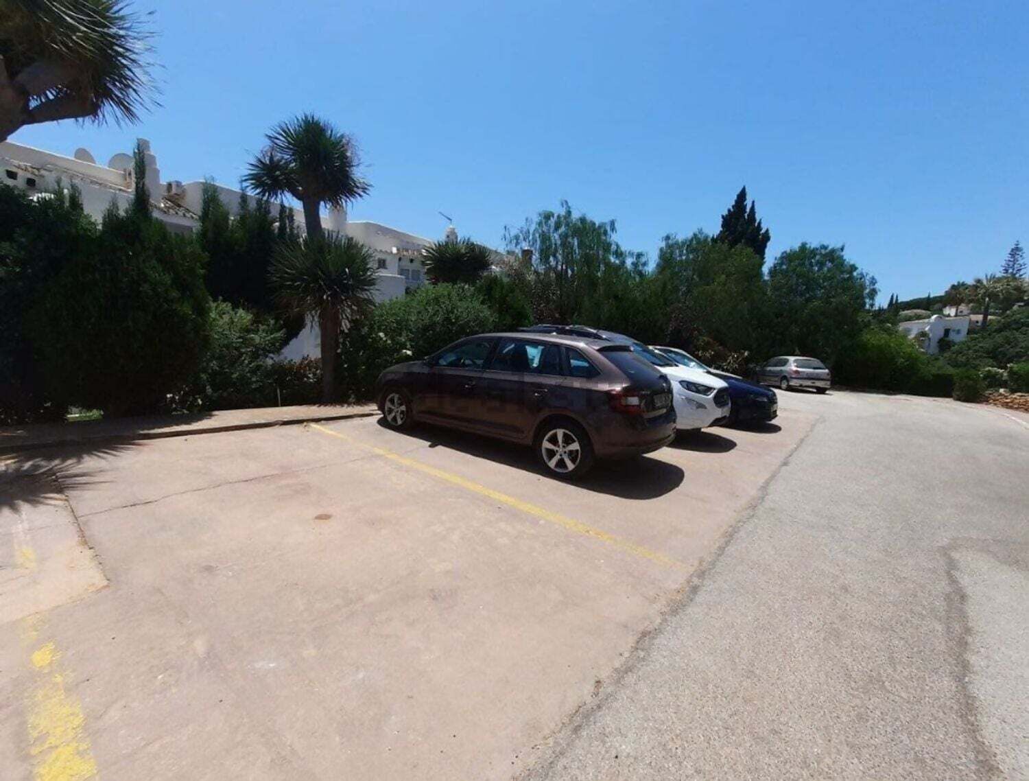 Un parking où sont garées plusieurs voitures, entouré de verdure et de bâtiments.