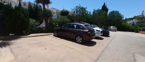 Ein Parkplatz mit mehreren parkenden Autos, umgeben von Grünflächen und Gebäuden.