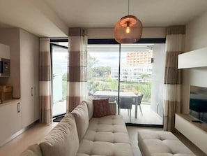 A modern living room with a sofa, a television, and a dining area visible through a glass door. - Torremar Luxe: upscale 2bed apartment by the beach (Torremolinos)