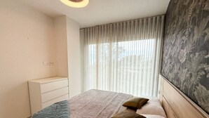Une chambre à coucher avec un lit, une table de chevet, une commode et une fenêtre avec des rideaux.