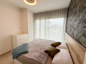 A bedroom with a bed, a bedside table, a dresser, and a window with curtains. - Torremar Luxe: upscale 2bed apartment by the beach (Torremolinos)