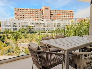 Ein Balkon mit Korbmöbeln, Blick auf ein mehrgeschossiges Gebäude und einen angelegten Garten.