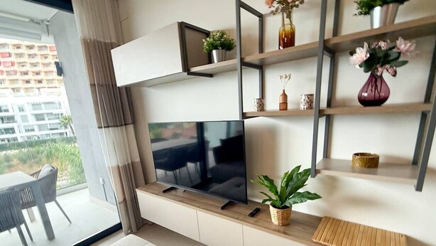 Un salon moderne doté d’un téléviseur à écran plat, d’un canapé, d’une table à manger et d’un balcon offrant une vue sur un immeuble.