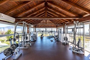 A gym with various exercise equipment, large windows, and a wooden ceiling. - Casa Cielo: One bedroom Apt with views in resort (Mijas)