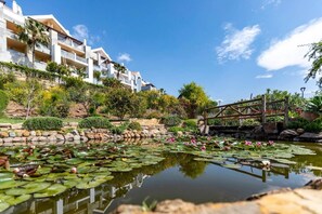 A serene garden with a pond, a wooden bridge, and a white building with balconies. - Casa Cielo: One bedroom Apt with views in resort (Mijas)